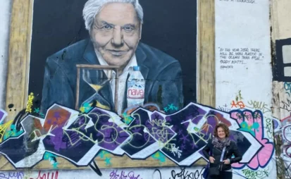 Lynn Griffiths in Margate, UK during Nov 2021, standing in front of a large graffiti image of Sir David Attenborough with his quote, “Industrial pollution and the discarding of plastic waste must be tackled for the sake of all life in the ocean”